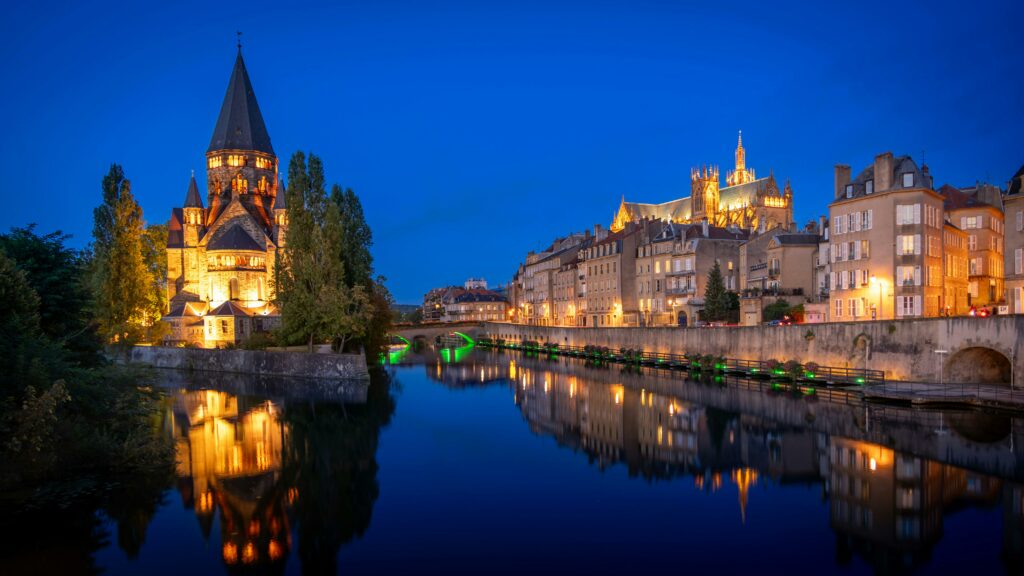 Captivating nighttime scene of Metz Cathedral and Moselle River reflecting city lights.